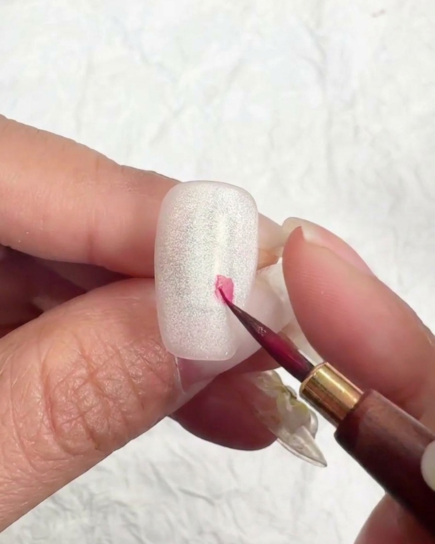 細い筆で爪にピンク色の点を描き、桜の配置を決めている様子