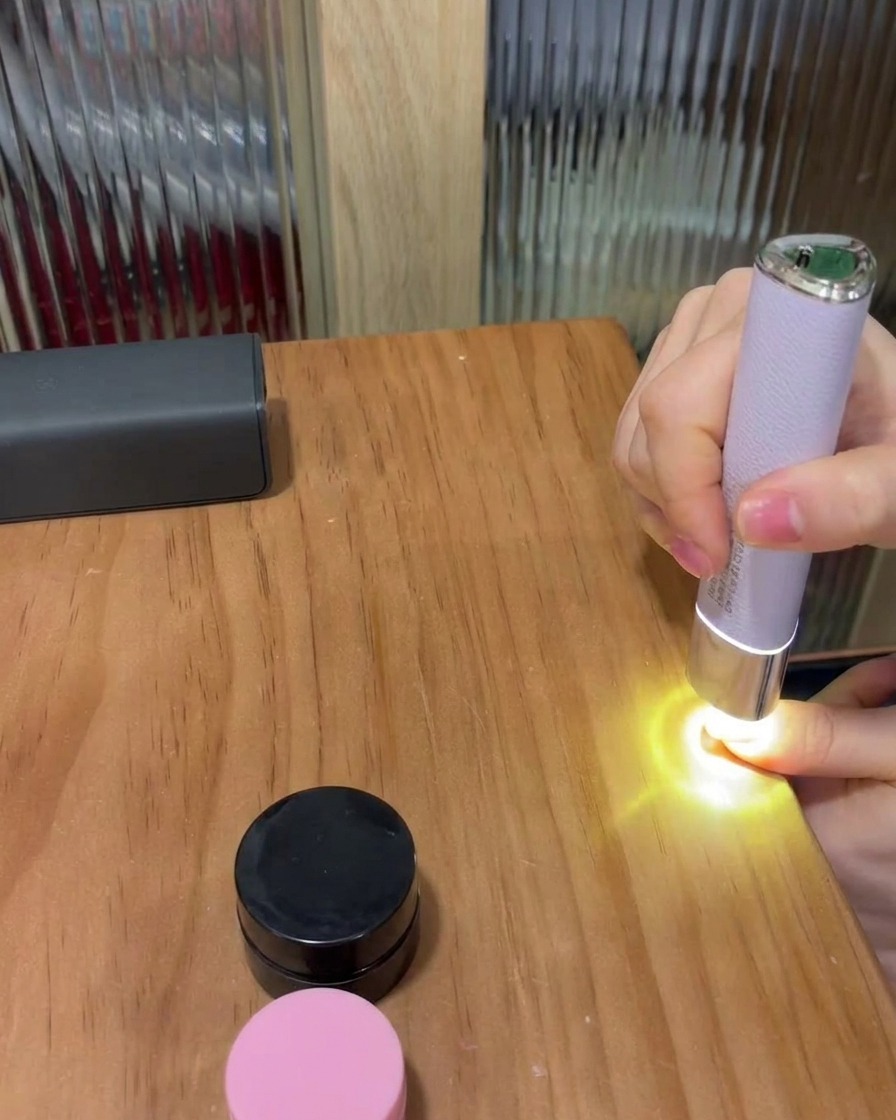 木製のテーブルの上で、小型のポータブル紫色のLEDランプの下に親指を置き、ジェルを硬化させている様子。