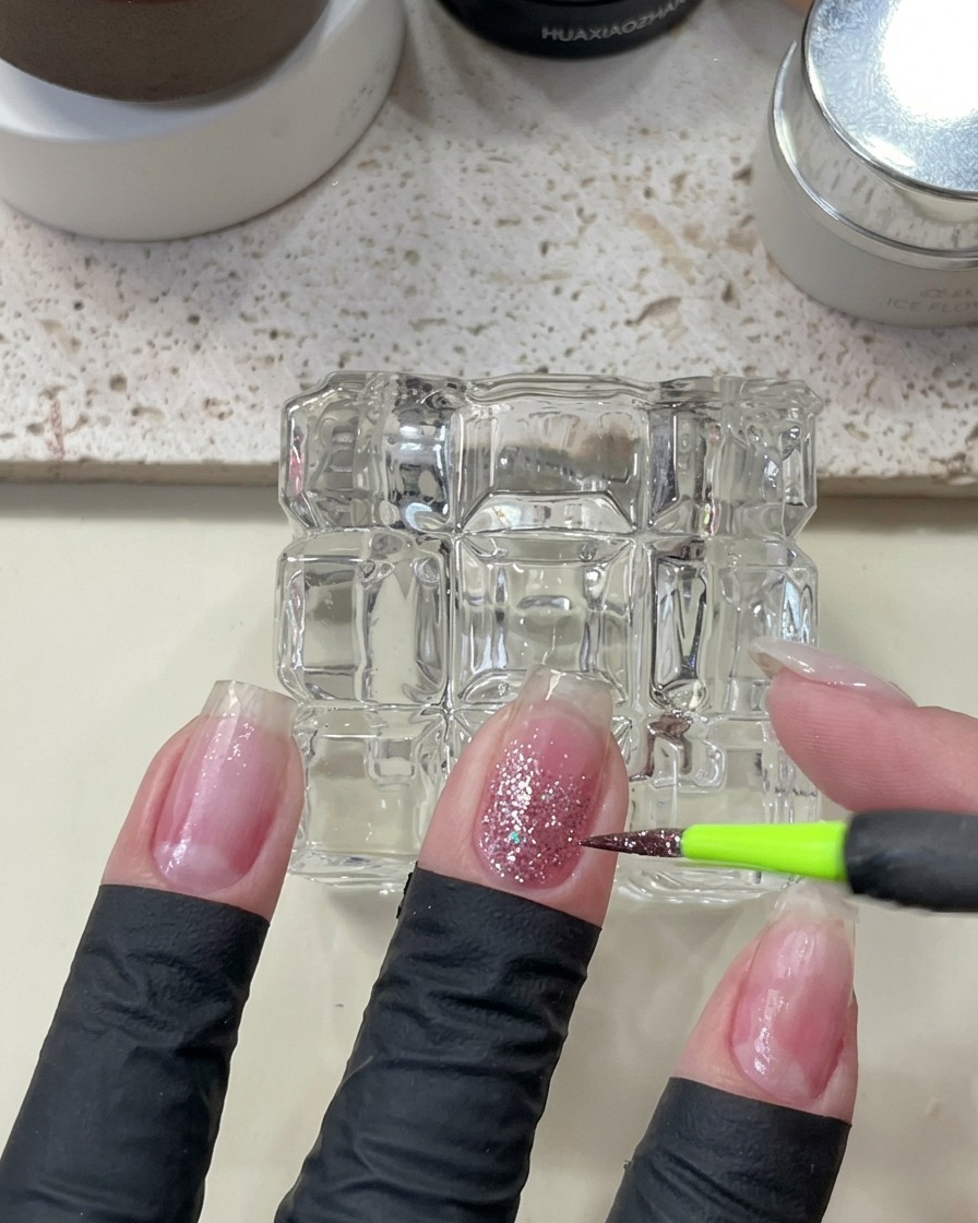 細い筆でピンク系のきらめくラメをグラデーションの上に重ね、輝きを足している様子。
