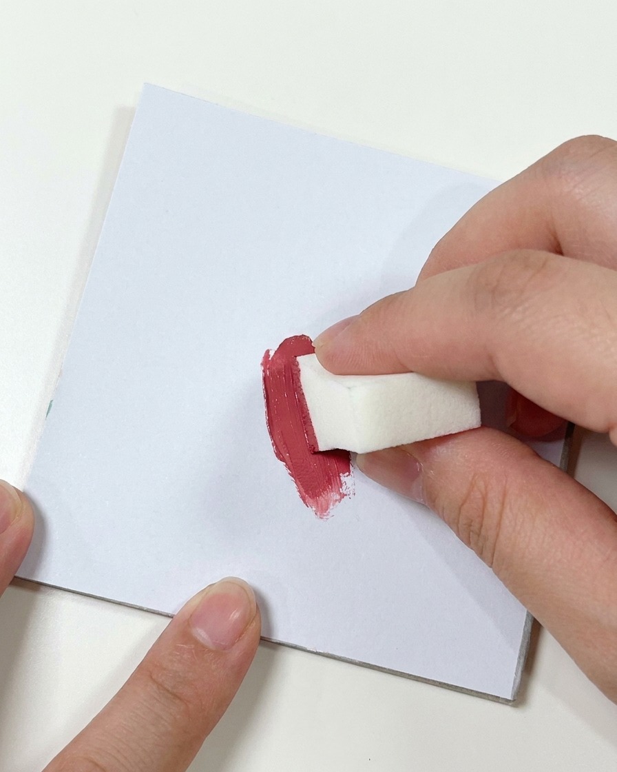 小さな白いメイクスポンジを、パレット上の濃いピンク色のジェルに押し当てている手。