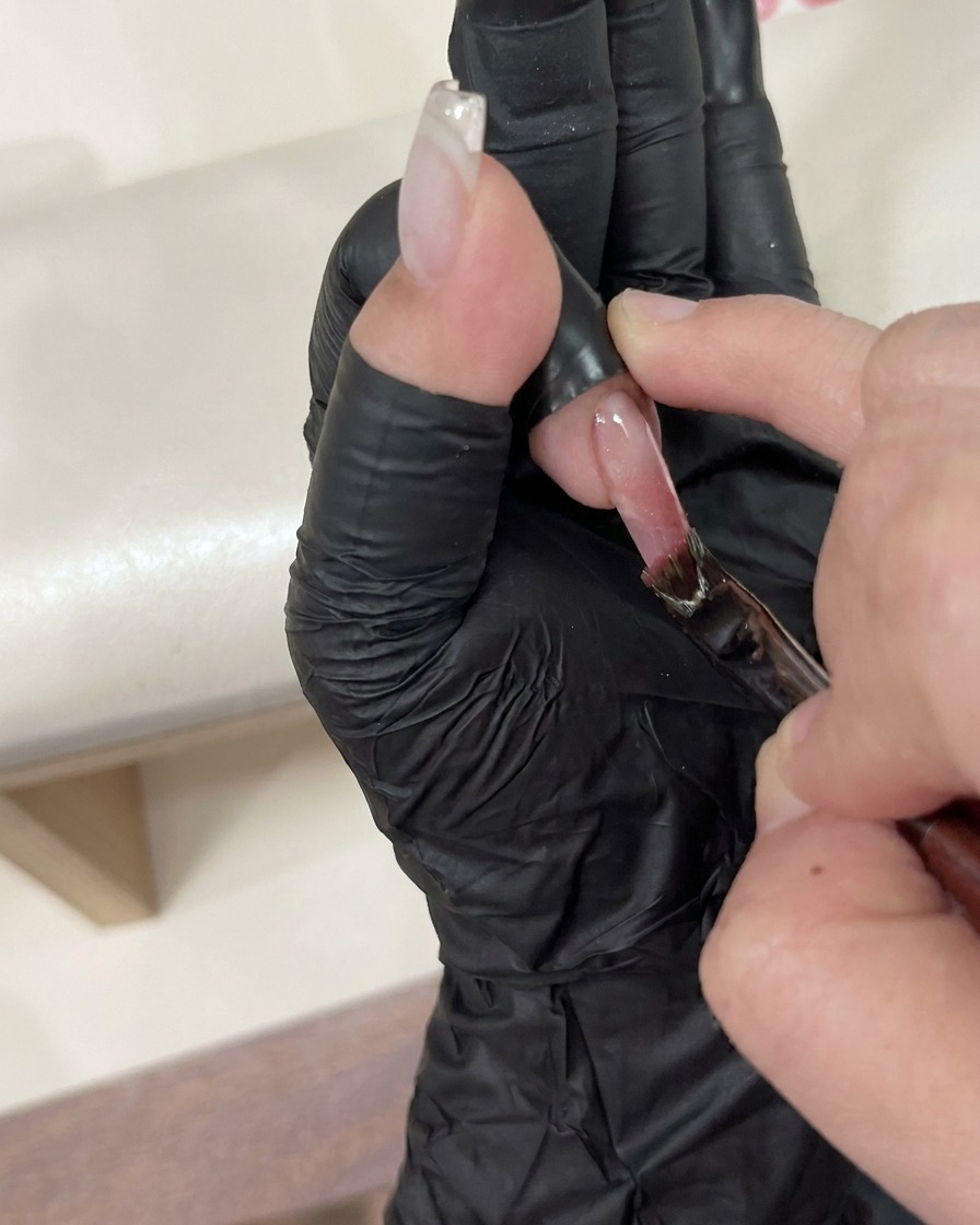 ピンセットを使って、トップコートが塗られた湿った爪の上に小さなチャームを置いている様子。