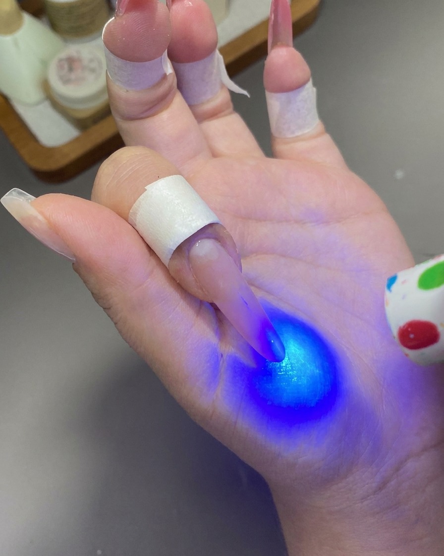 ミニサイズのハンディUV/LEDライトで、爪のジェルを硬化させている様子。