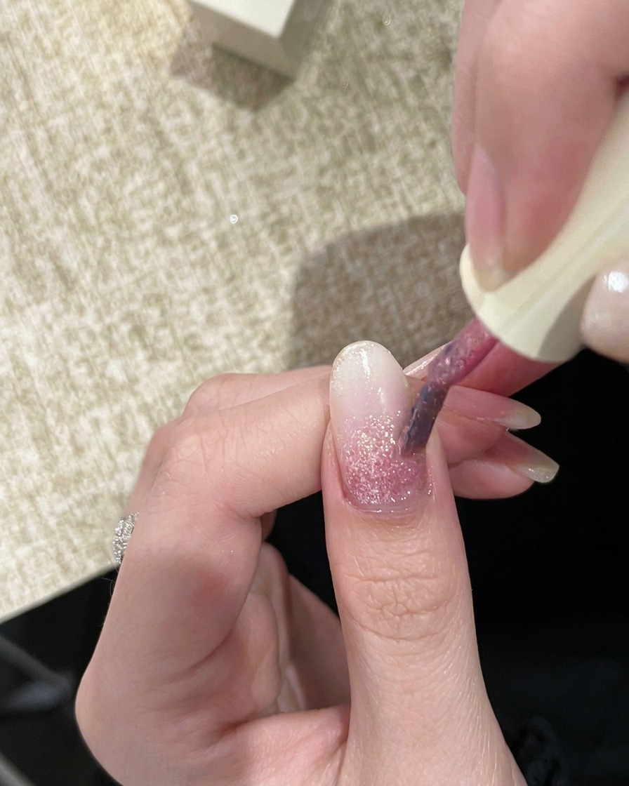 先ほどより濃いピンクのラメジェルを筆で爪に乗せている様子。