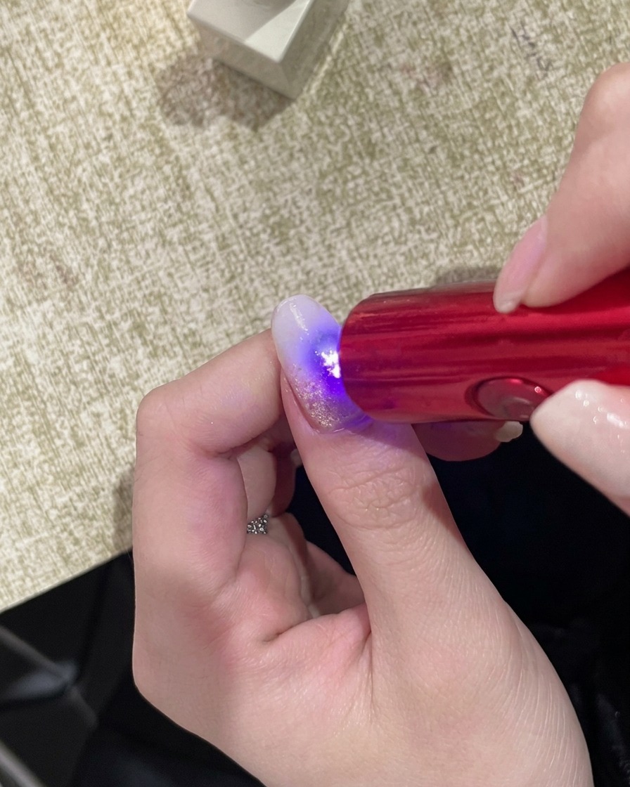 ハンディUVライトの下で爪の表面が光を反射している様子。