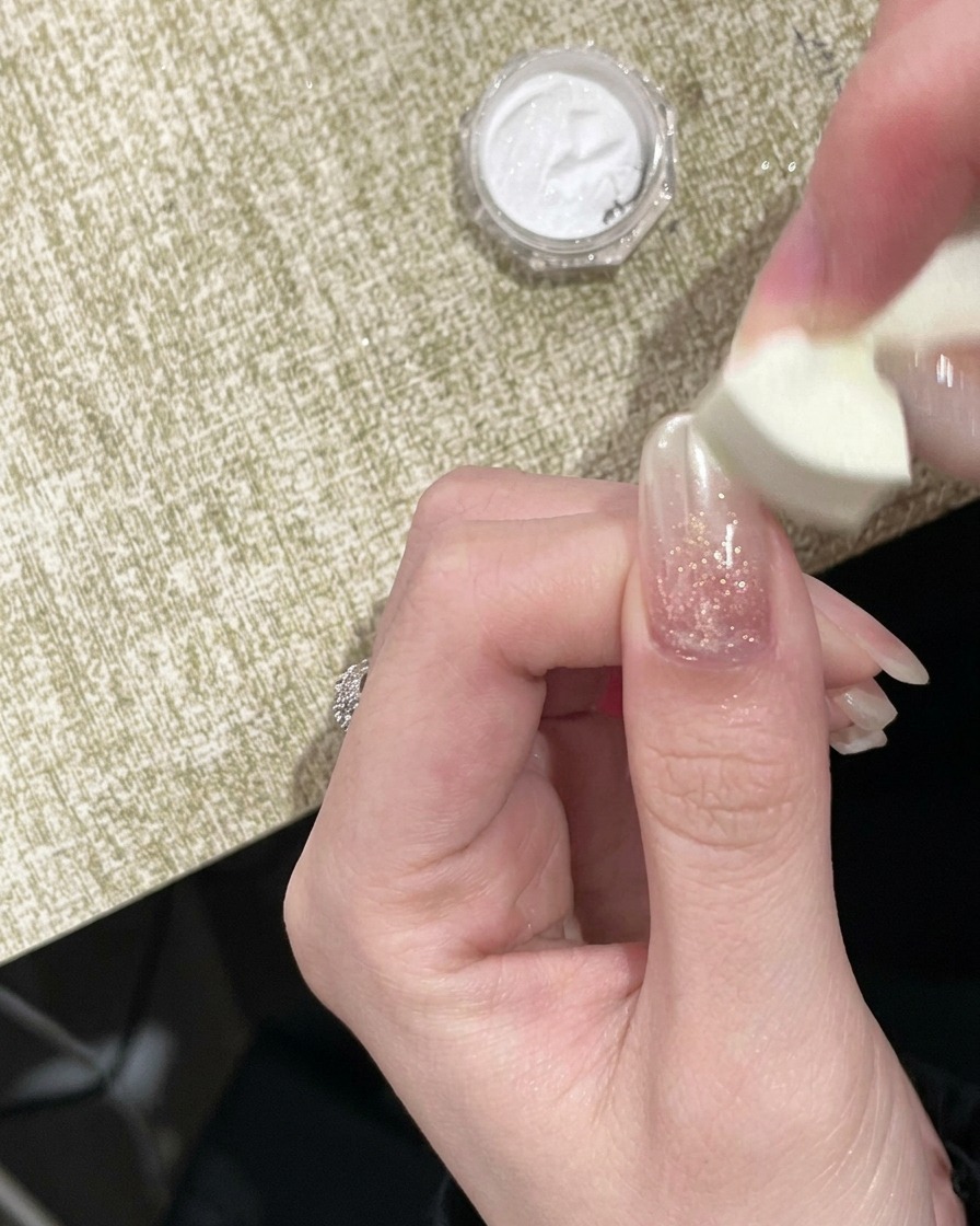 スポンジチップで爪先にゴールドのミラーパウダーを擦り付けている様子。