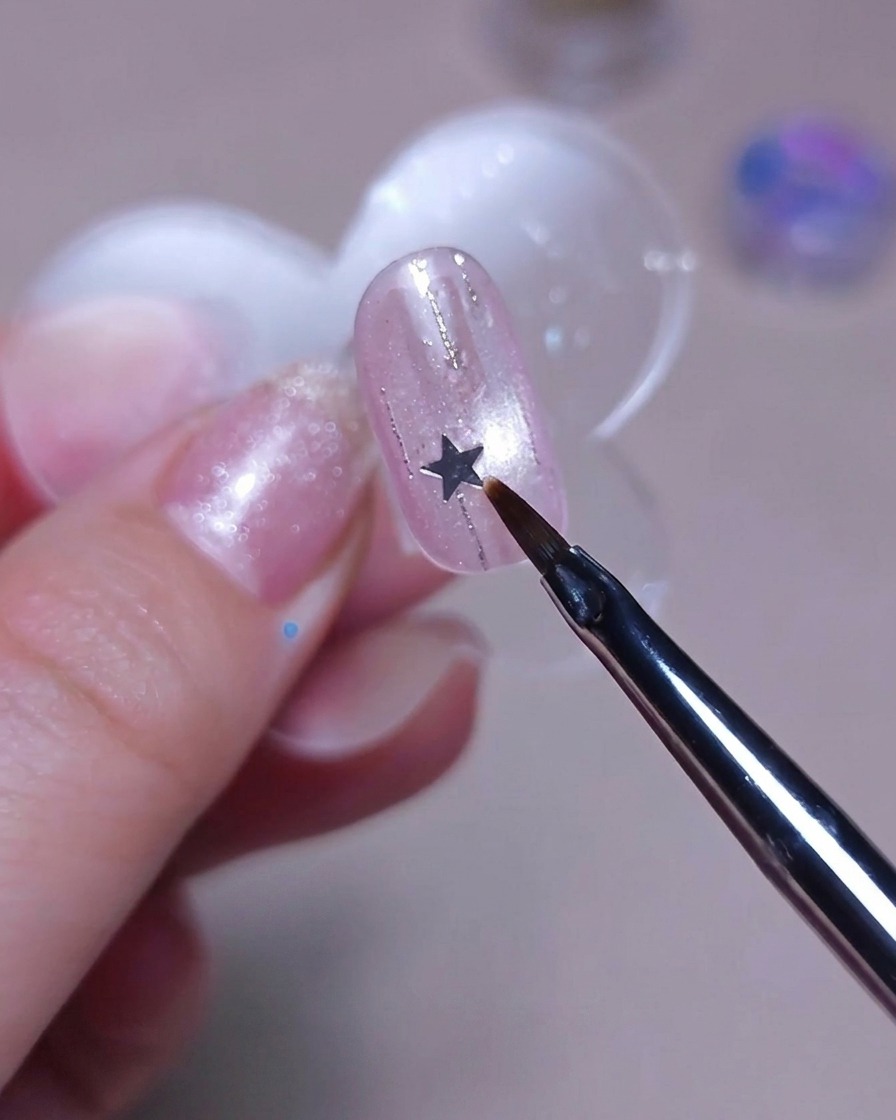 細筆の先でシルバーの星のスタッズを爪の上に置いている様子。