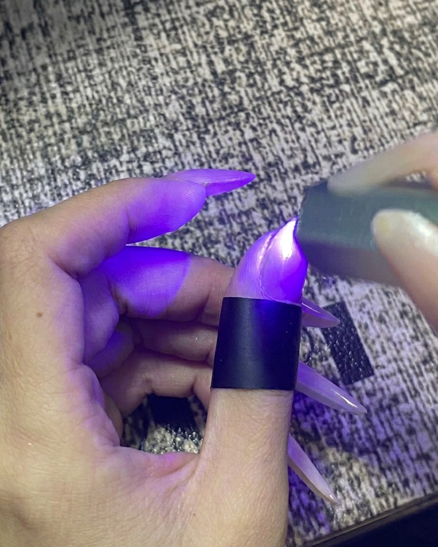 ライトが点灯しているポータブルUV/LEDネイルライトの中に指を入れている様子。
