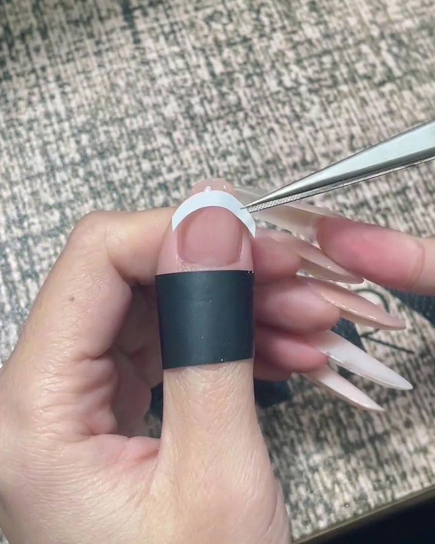 ピンセットを使って、爪の中央に白いカーブ状のフレンチガイドシールを水平に貼っている様子。