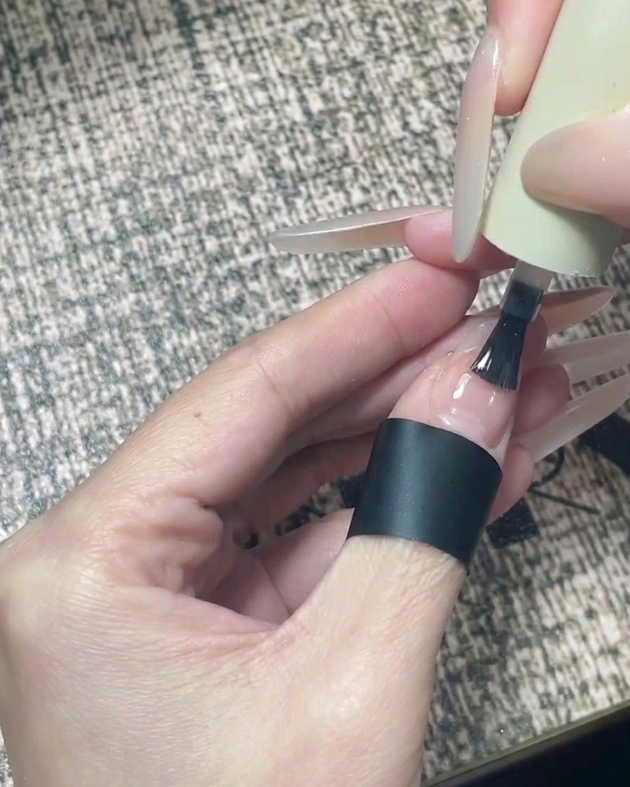 黒い星をあしらった完成したネイルデザインに、クリアな艶出しトップコートを塗っているブラシの様子。