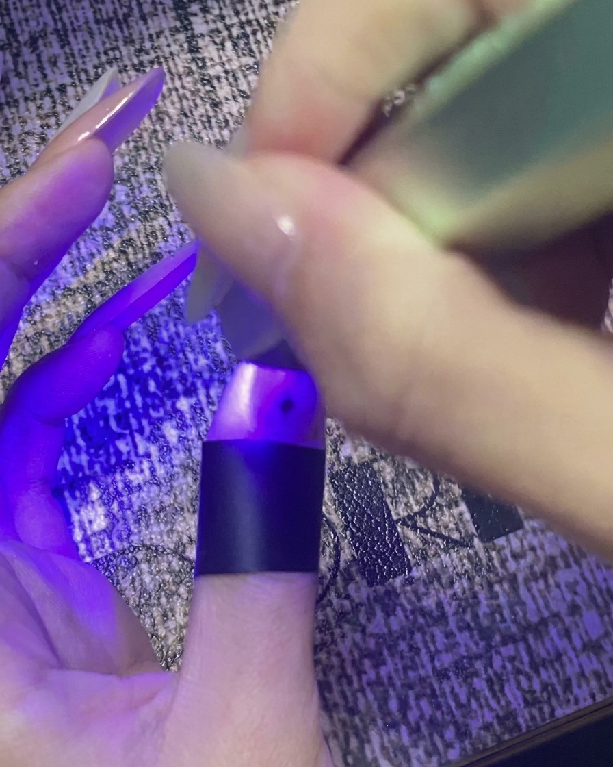 星のネイルアートが施された親指を、紫色のミニUV/LEDライトの下で硬化させている様子。