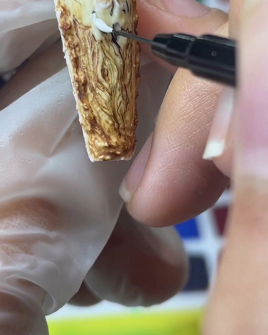 細いブラシでホワイトサンドジェルを使い、茶色の背景の上に立体的なバラの花びらを描いている様子。