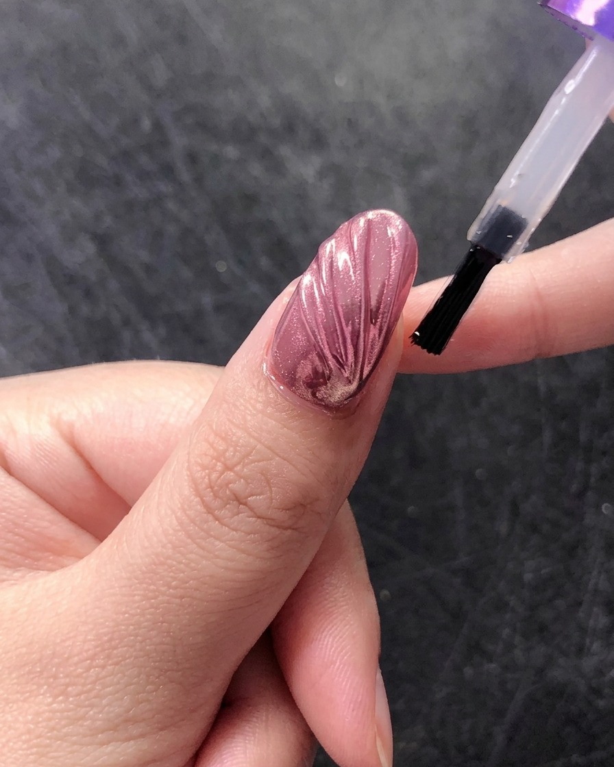 クロム仕上げのシェルネイル全体に、艶出しのトップコートを筆で塗っている様子。
