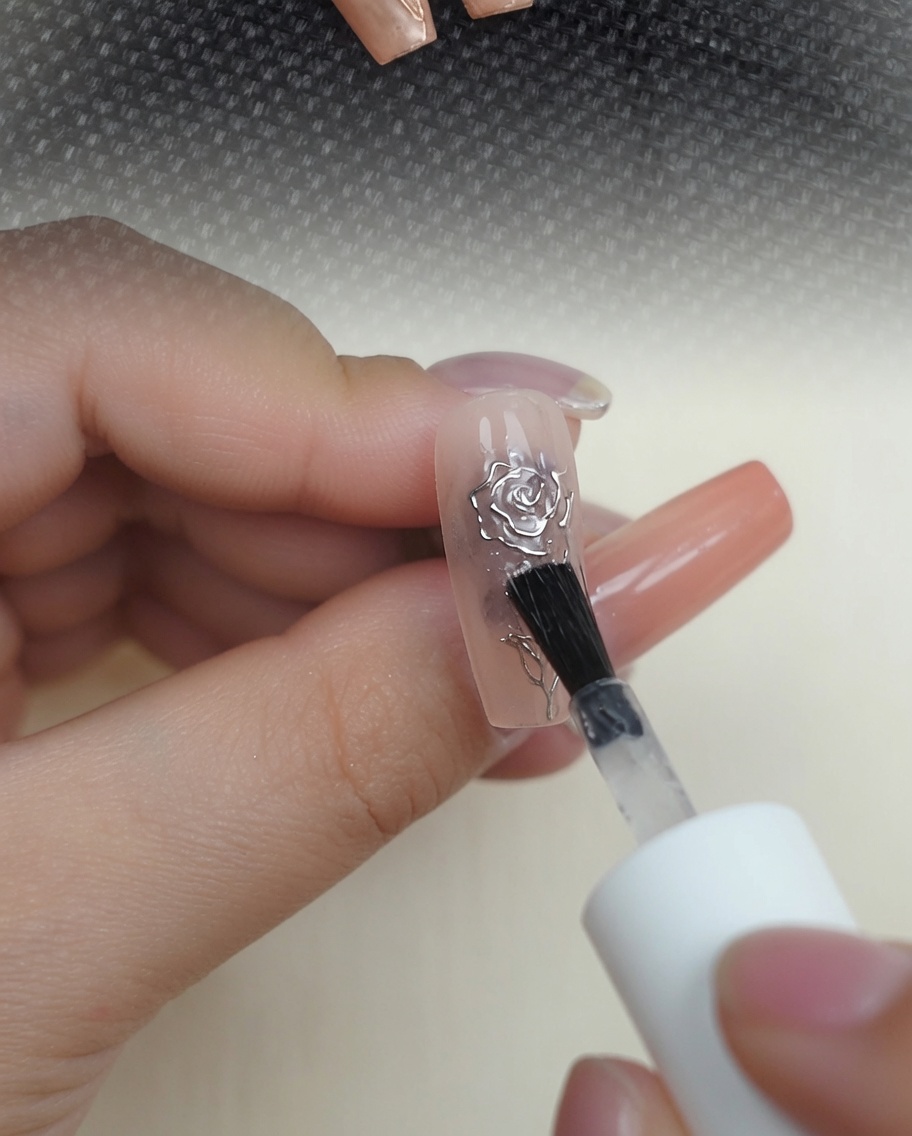 メタリッククロムの3Dローズネイルの上に、クリアな光沢トップコートを塗布している様子。