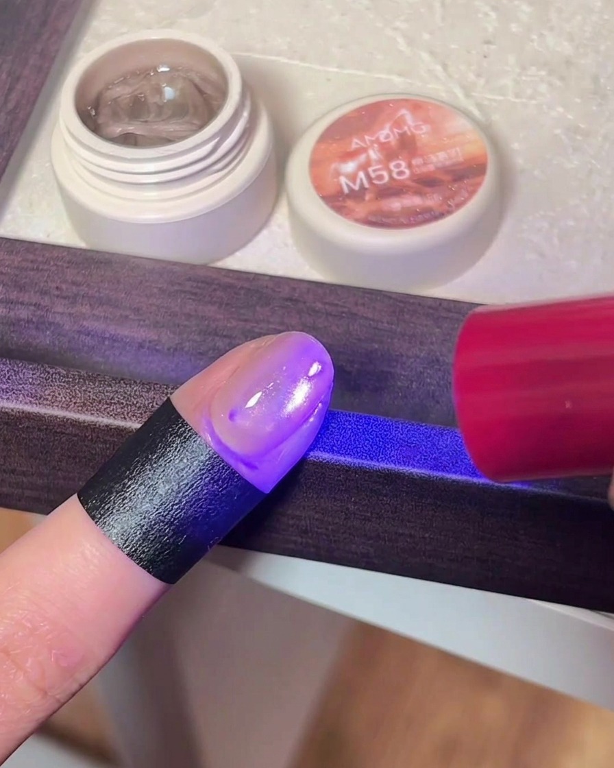 UV/LEDネイルライトの紫色の光の下でマグネットジェルを硬化させている指のアップ。