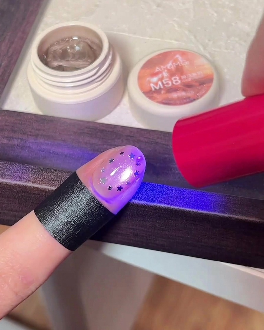 星のホログラムを乗せた指をUV/LEDライトで硬化させている様子。