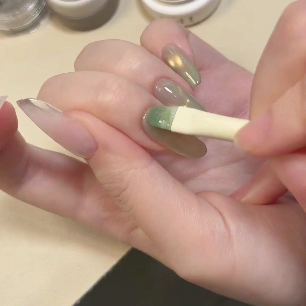 透明感のあるレイクグリーンのキャットアイジェルを、爪全体に塗布している筆。