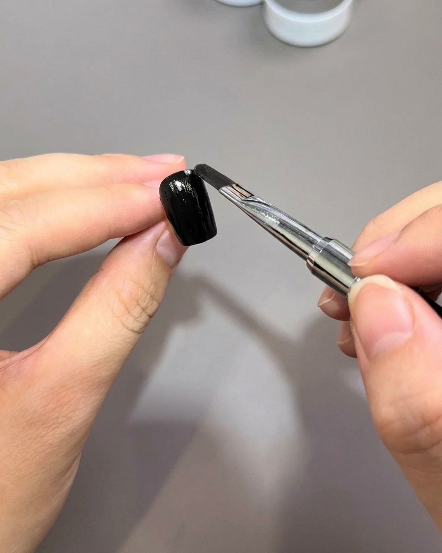 下準備をした爪の表面に、黒のジェルポリッシュを滑らかに塗布しているネイルブラシ。