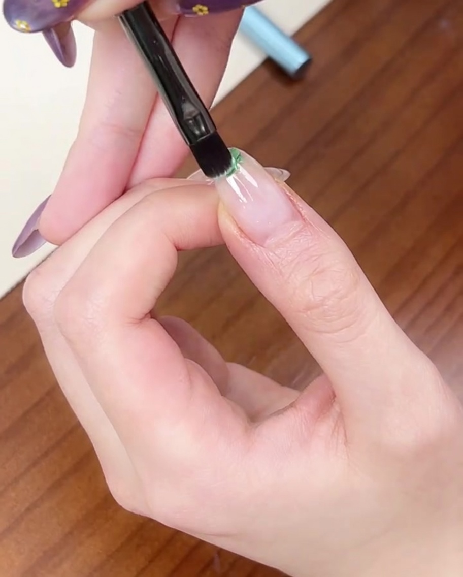 平筆を使い、自爪の先端に少量のライトグリーンジェルを乗せている様子。