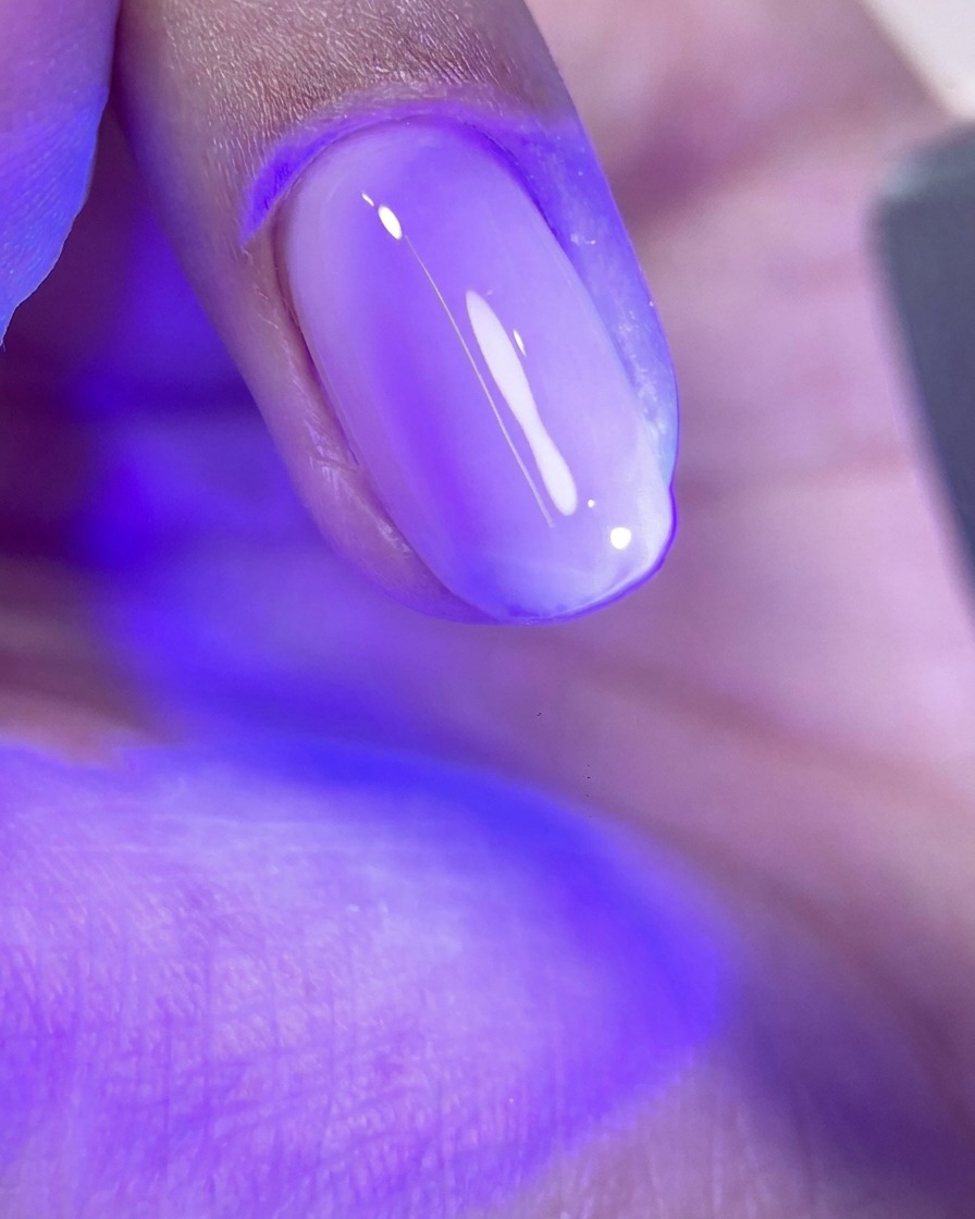 ピンクのジェルが塗られた爪が、UV/LEDランプの紫色の光の下で硬化されている様子。