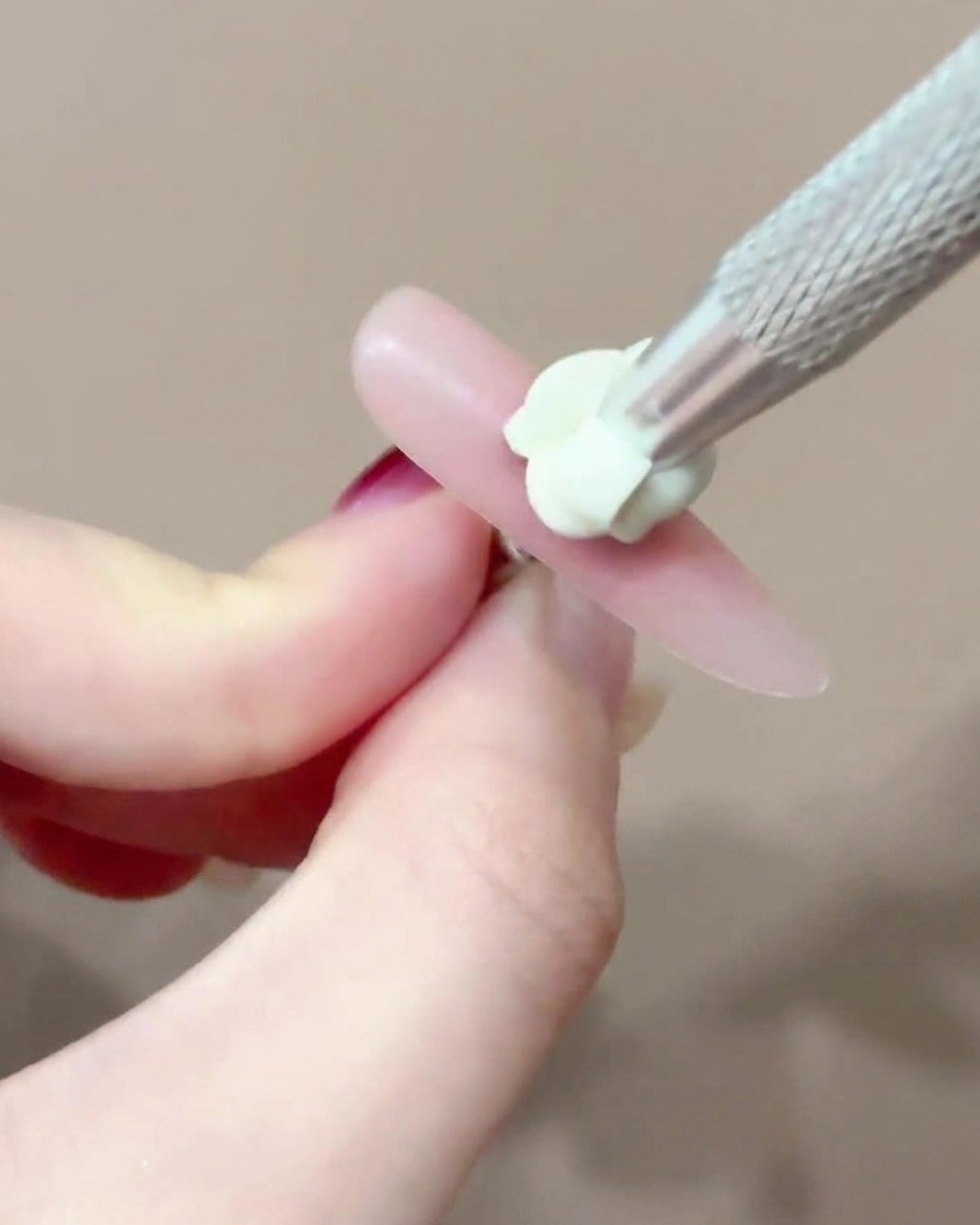 細筆を使って爪の中心に小さなピンクのチークジェルのドットを正確に置いている様子。
