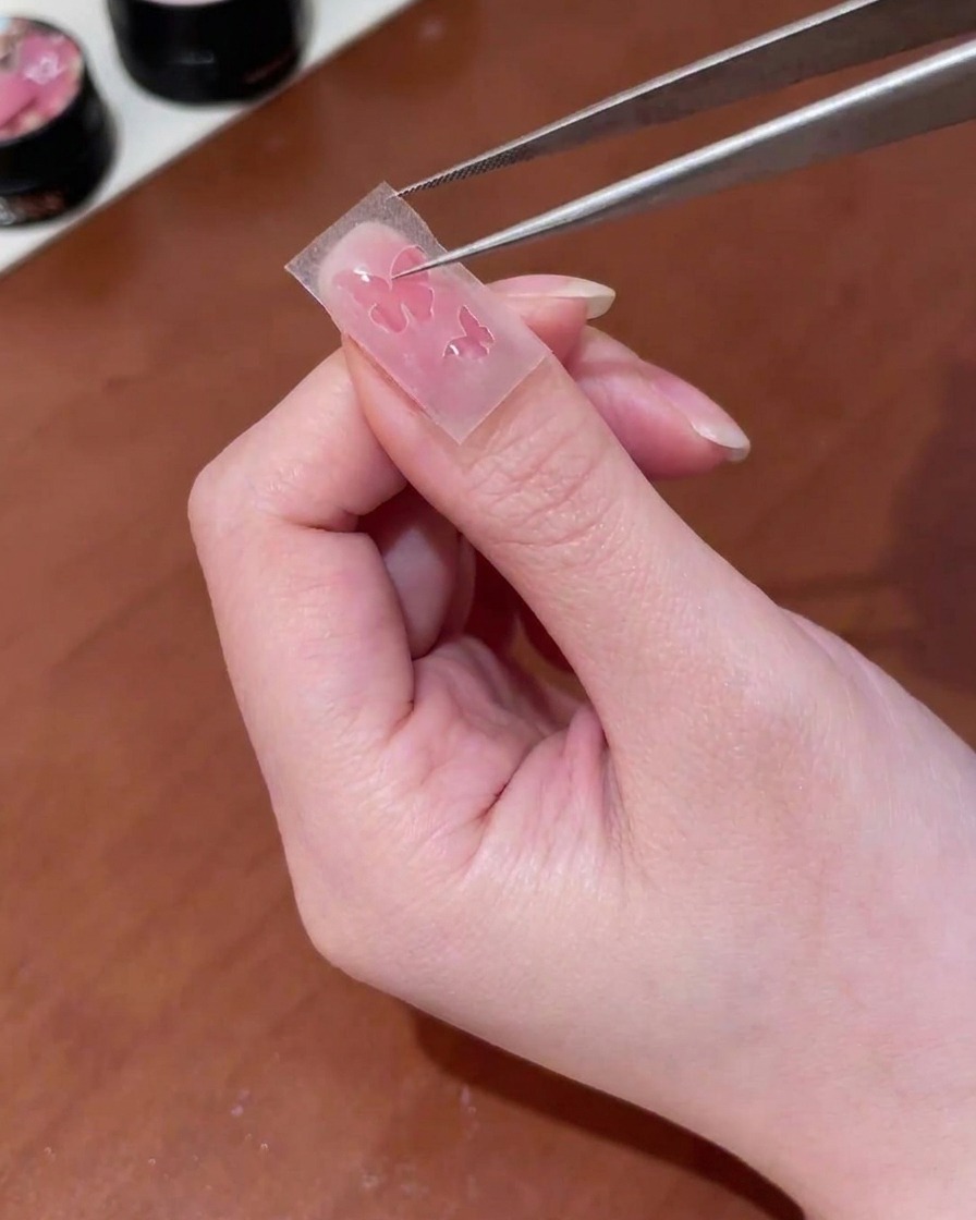 ピンセットでバタフライ型の切り抜きステッカーを爪の中央に配置している様子。