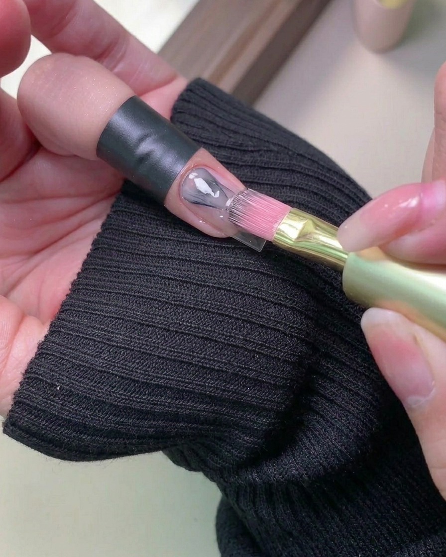 自爪に柔らかい薄い色のジェルネイルを筆で塗布している様子。