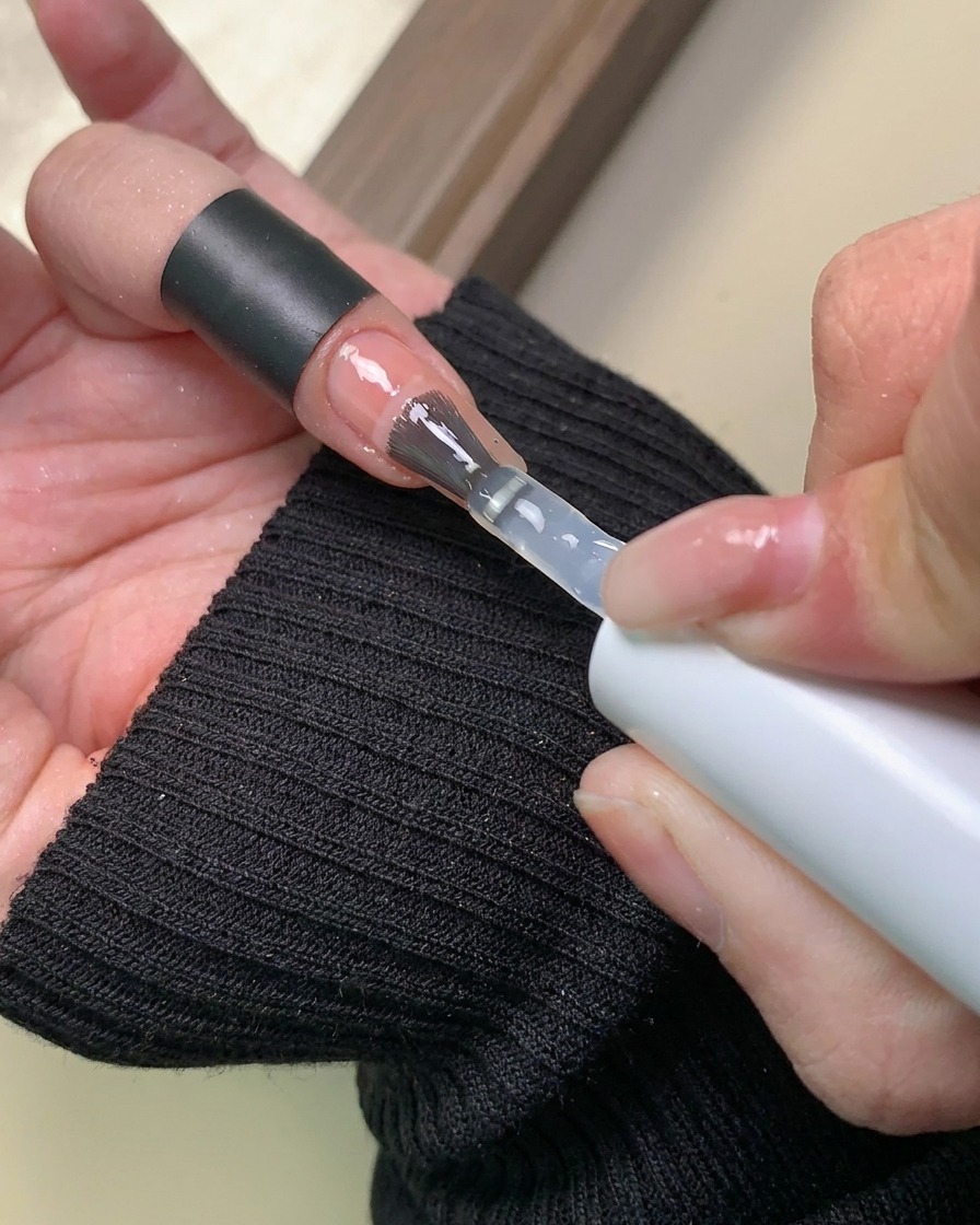 パウダーデザインの上に、透明なベースジェルを筆で塗布している様子。