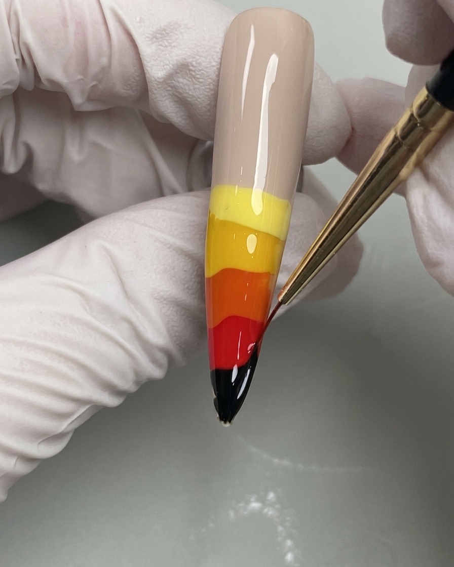 細いライナーブラシでウェットなジェルを根元に向かって引き上げ、炎の形を作っている様子。