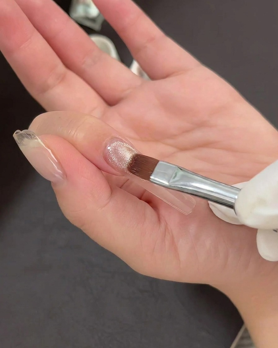 ネイルアート用の筆で、クリアなネイルチップにキャットアイジェルを薄く塗っている様子。