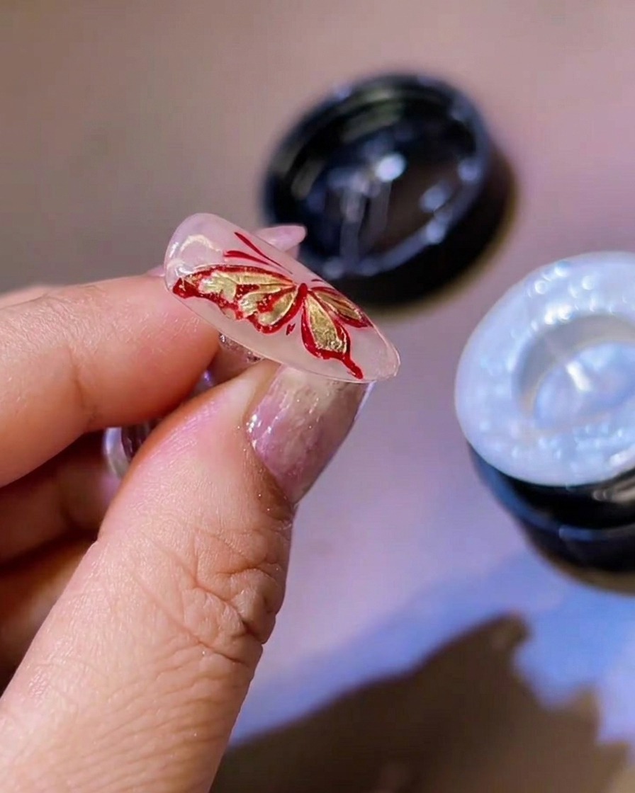 極細ライナー筆を使って、3Dの蝶の羽の縁に白いジェルで細かなディテールを加える様子。