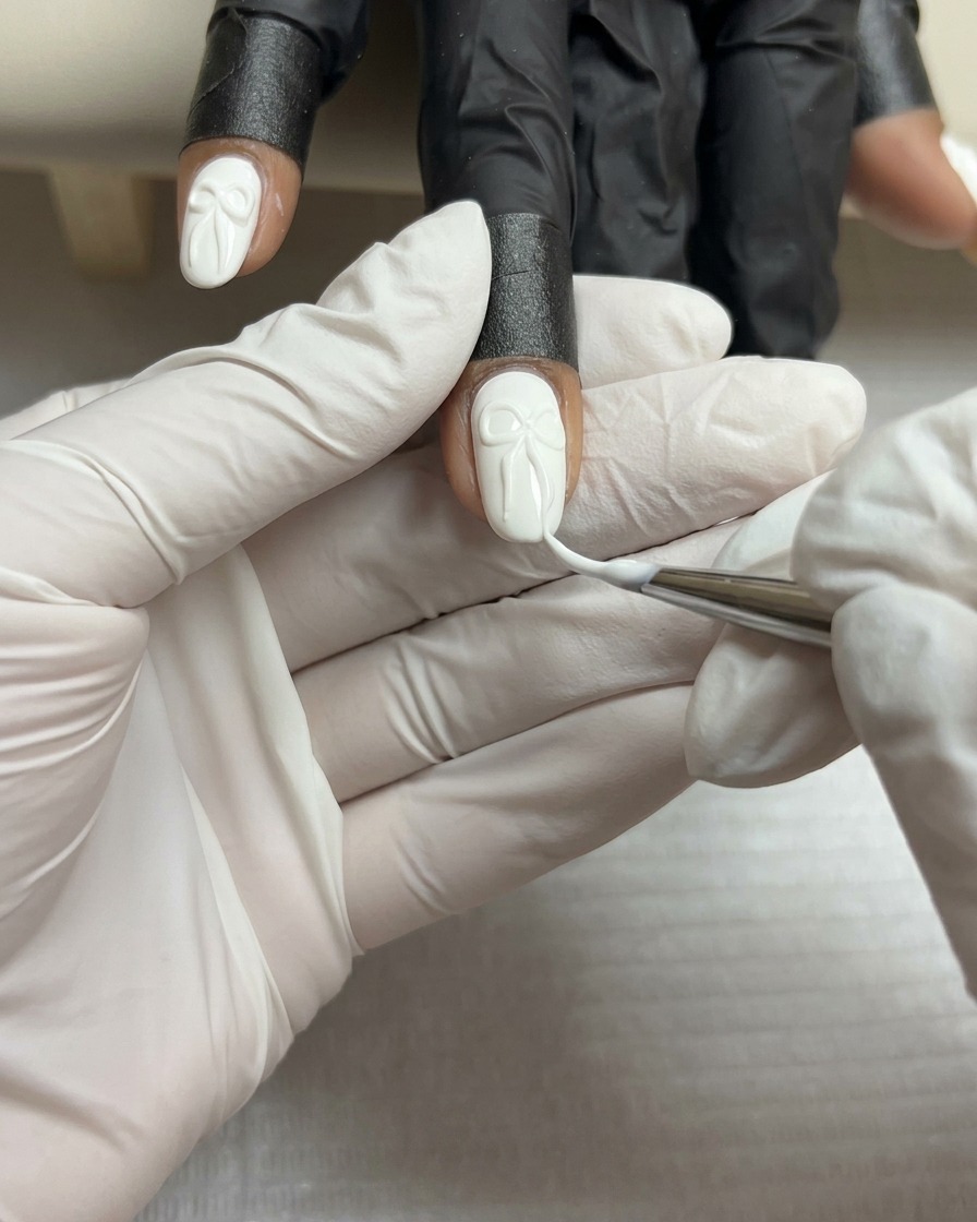 ホワイトネイルの上の3Dリボンに、極細ライナーブラシで薄いホワイトのラインを描き込んでいるアップ画像。