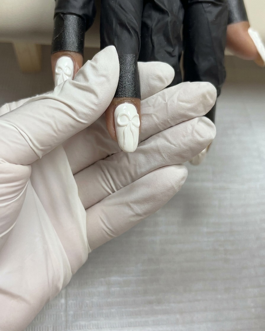 最終硬化前の、ホワイトネイルに施された完成した3Dジェルリボンデザインの俯瞰図。