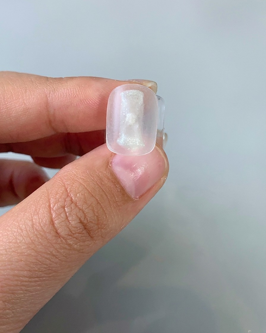 薄い色のキャットアイジェルをネイルチップにブラシで塗布している様子。