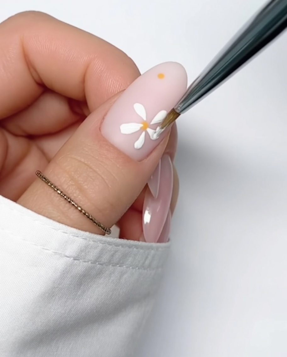 ヌードカラーのネイル上に、2つ目の花の中心となる小さな黄色のドットが描かれている様子。
