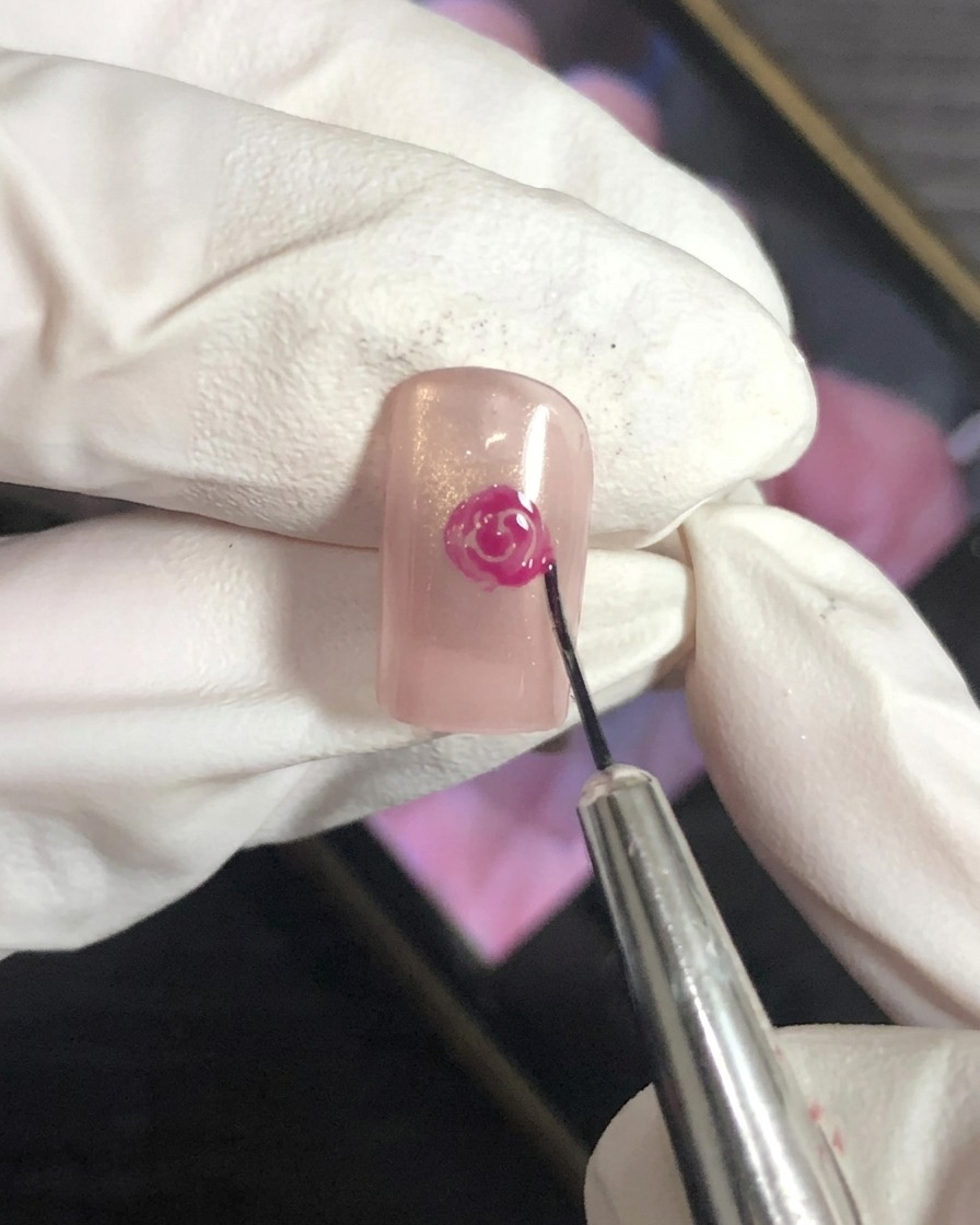ネイルアート用の筆を使って、ベースの上でマゼンタの花びらの端をぼかしている様子。