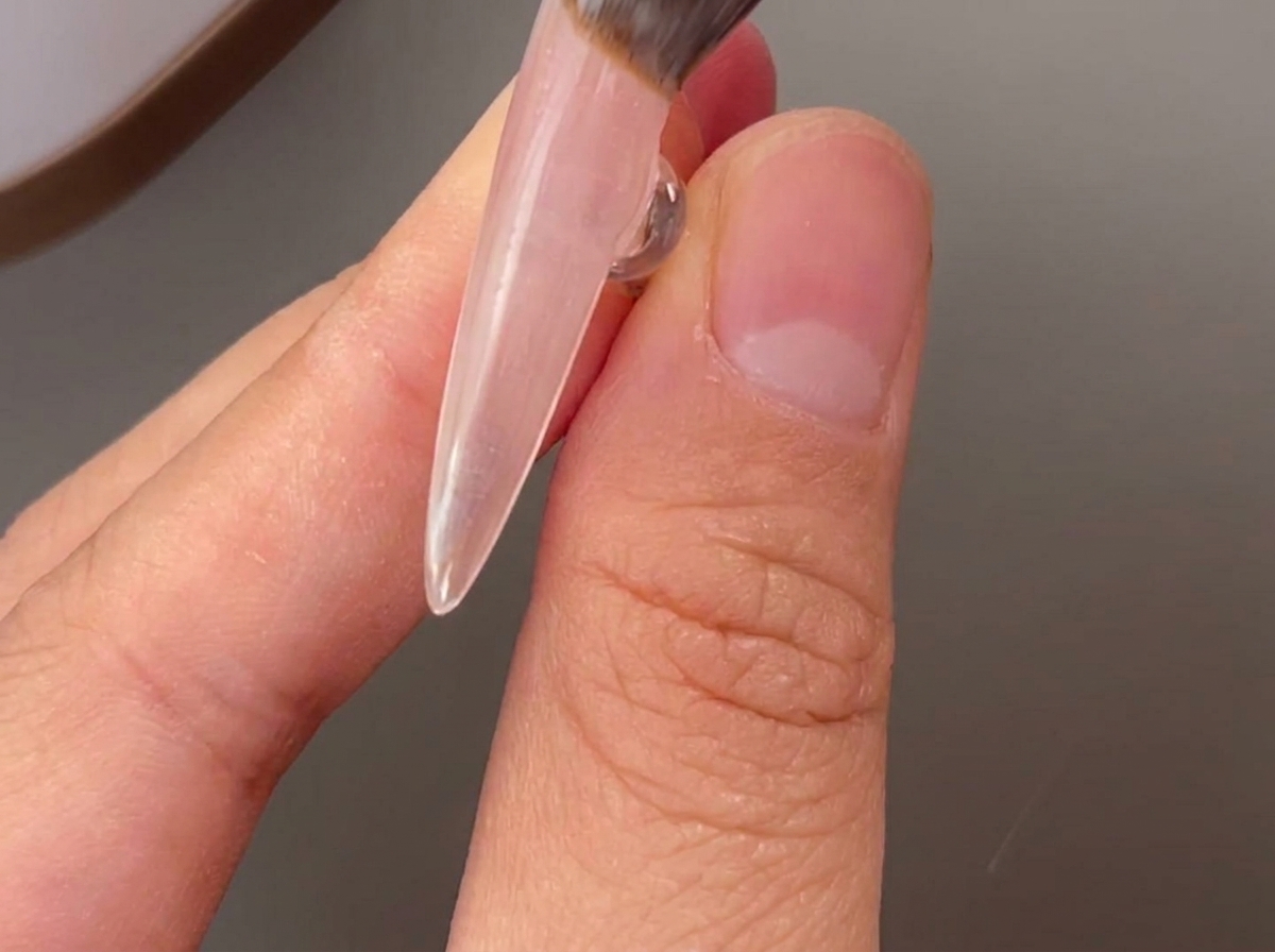 自爪にクリアなベースジェルを筆で塗布している様子。