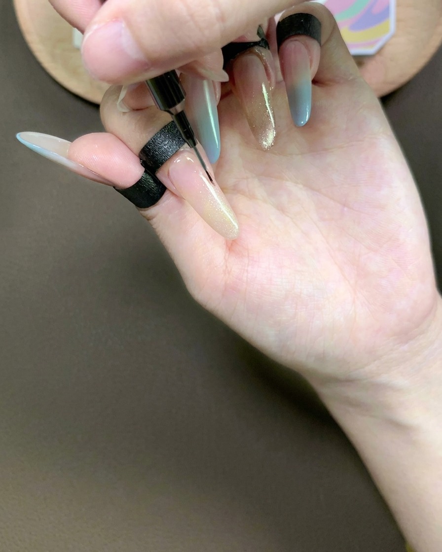 細いライナー筆で人差し指のキャッツアイジェルを優しく引き、滑らかなグラデーションを作っている様子。