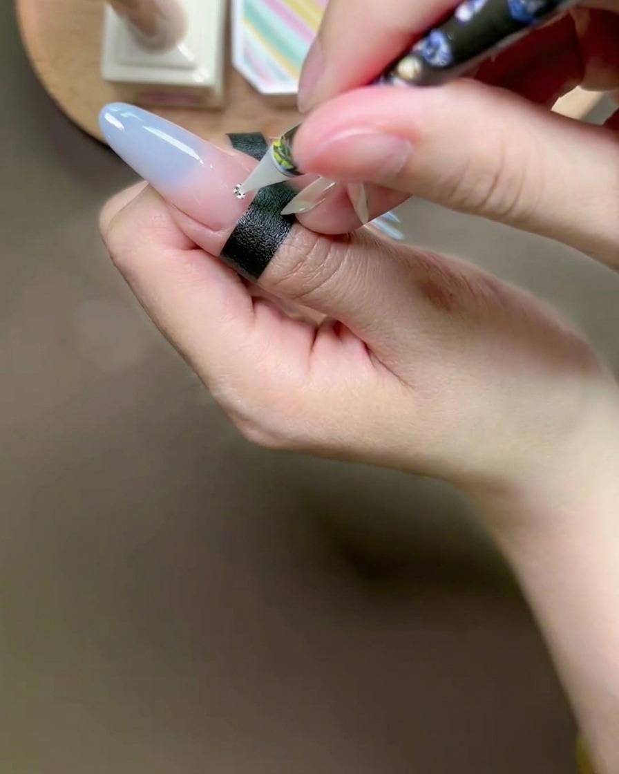 ワックスペンを使って、爪の上のグルーに小さなシルバーのラインストーンをのせている様子。