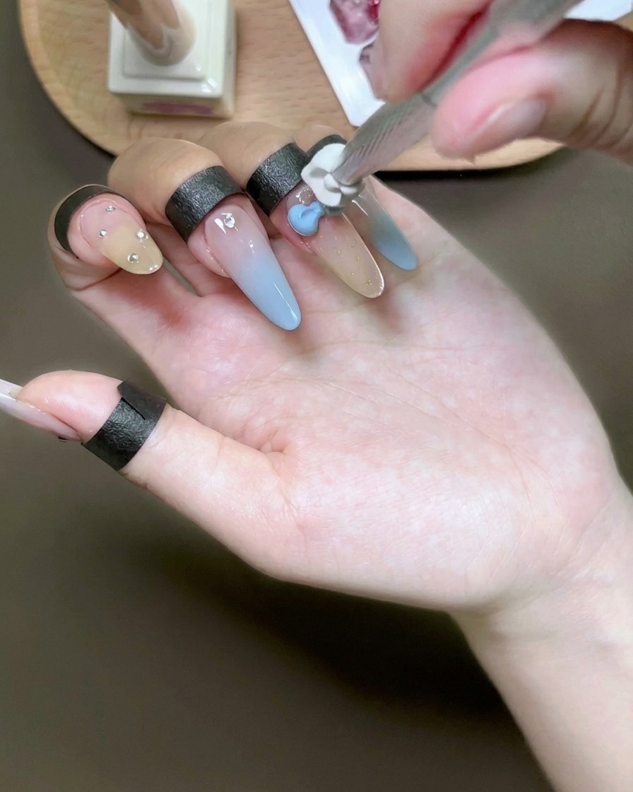 スポンジツールを使って、爪の上の白い3Dリボンチャームにライトブルーのジェルを叩き込んでいる様子。