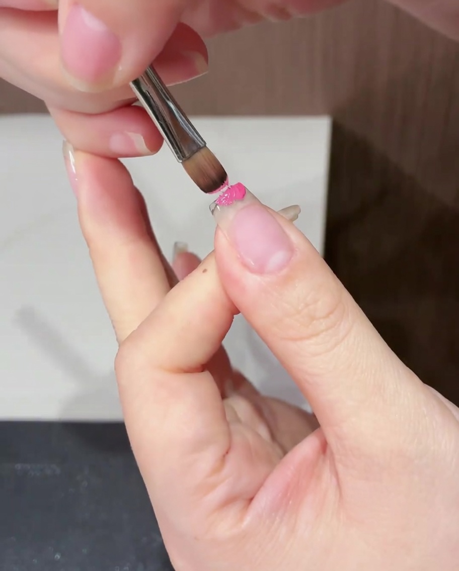 平筆を使い、爪の先端部分にのみマゼンタのジェルを塗布している様子。