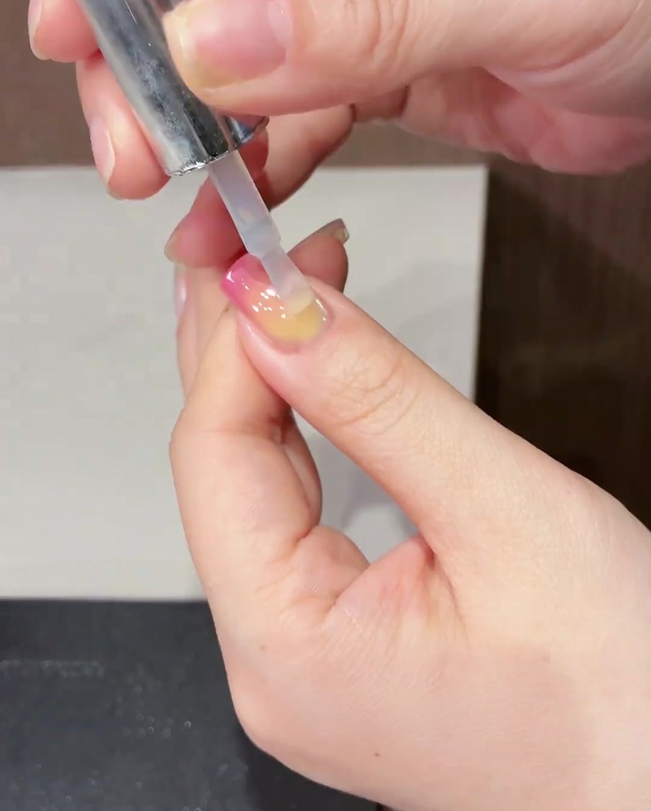 完成したチューリップネイルの上に、透明で艶やかなトップコートを筆で塗布している様子。