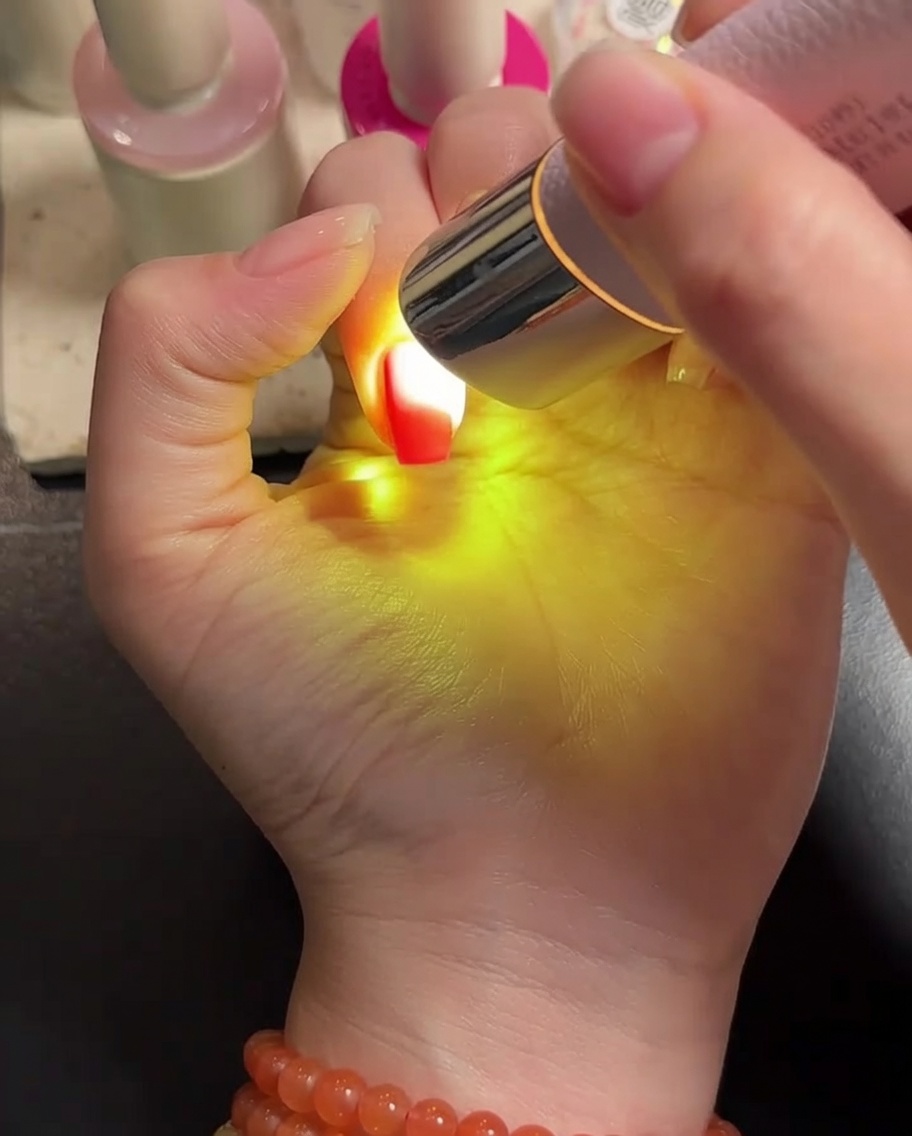 LEDライトの下でピンクのジェルを塗った指を硬化させている様子。