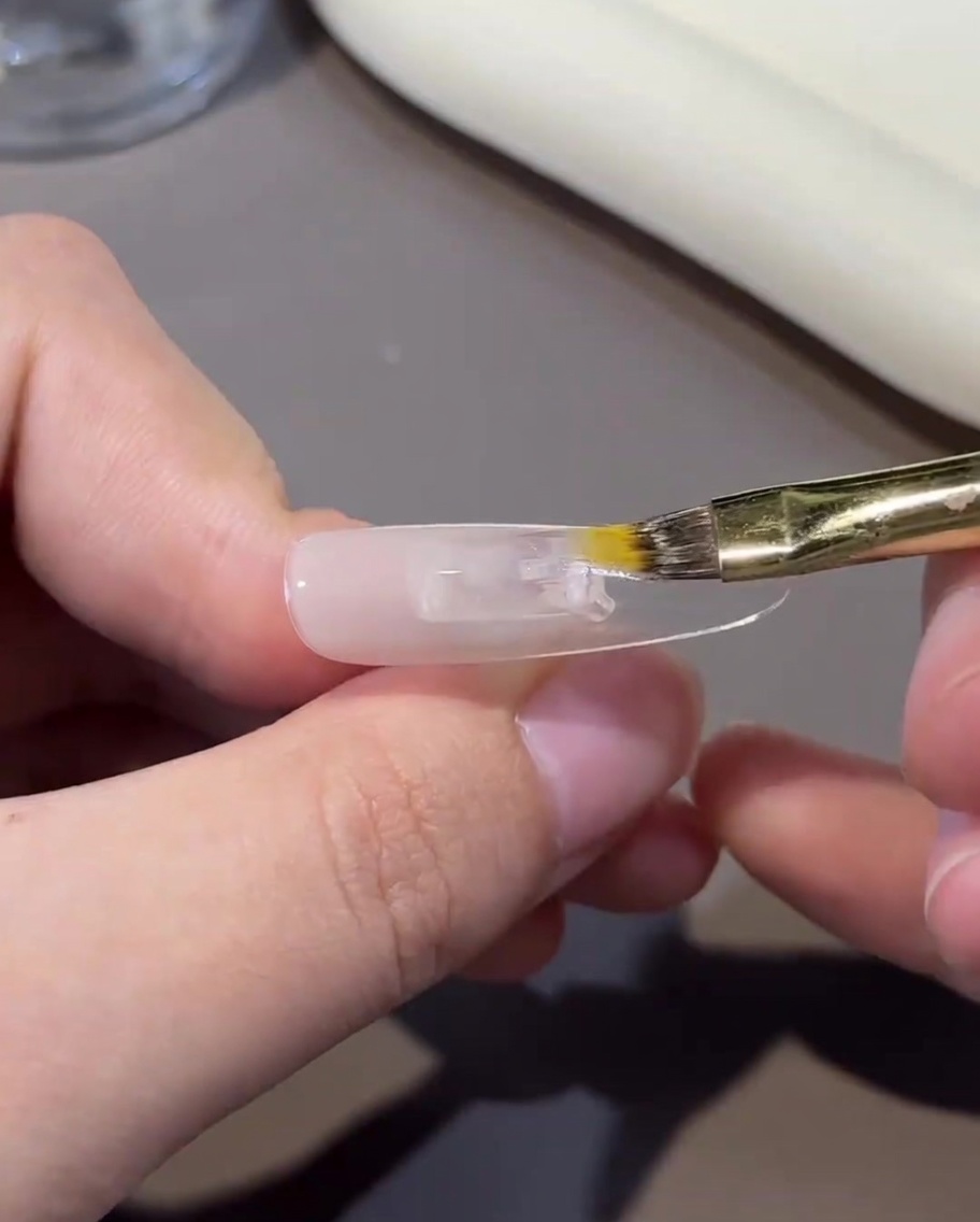 筆を使って爪の表面のヌードジェルを軽くぼかし、グラデーションを作っている様子。