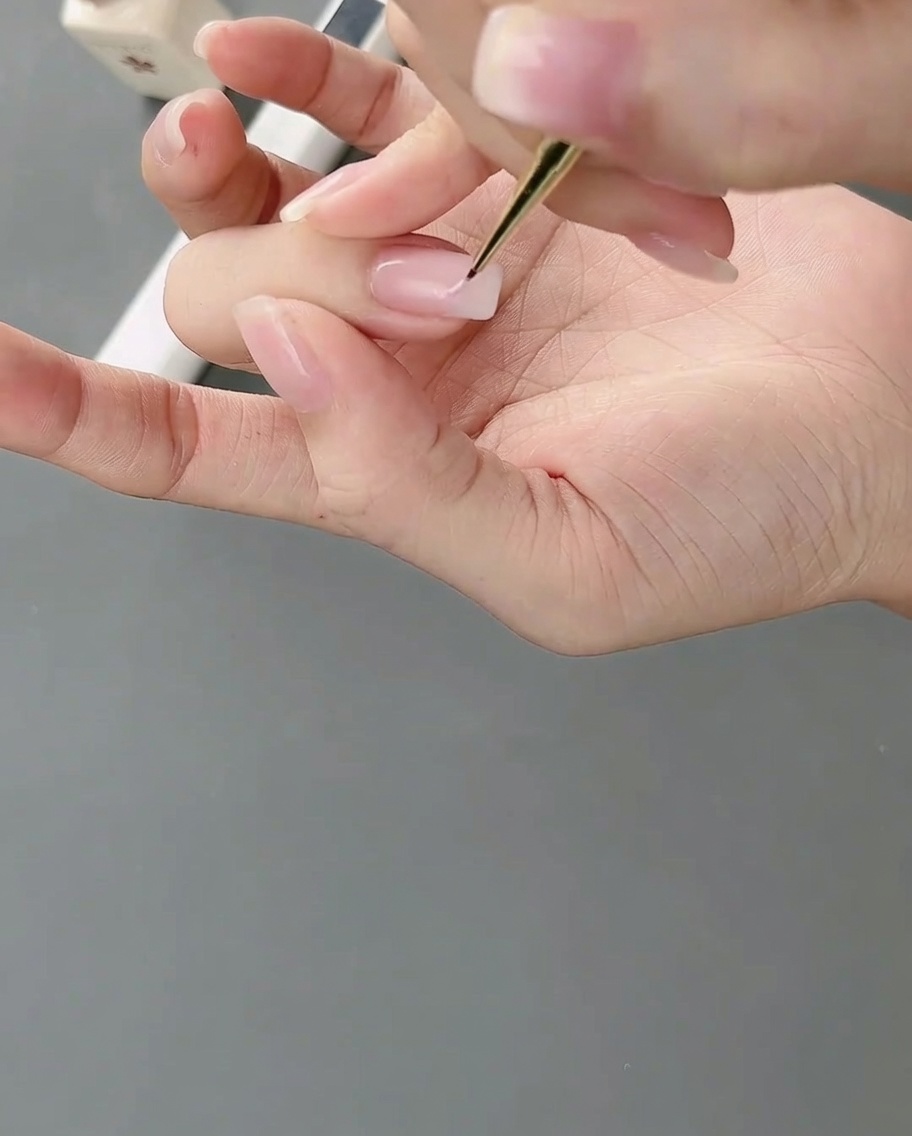 細いネイルアートブラシで爪にライトピンクのジェルを塗り、不規則なカラーブロックを作る様子。