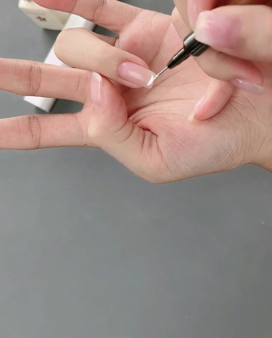 ライナーブラシで爪の先端に白いジェルを塗り、高めのフレンチラインを作っている様子。