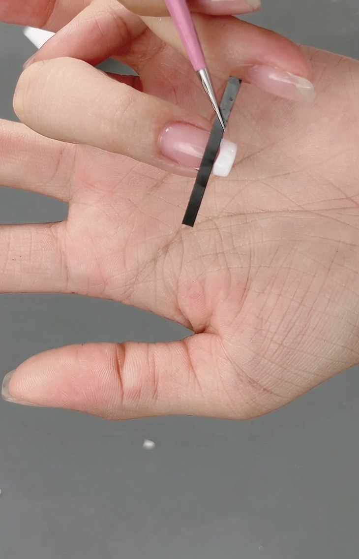 フレンチネイル用のステッカーを爪の先端に貼り、格子柄のガイドを作っている様子。