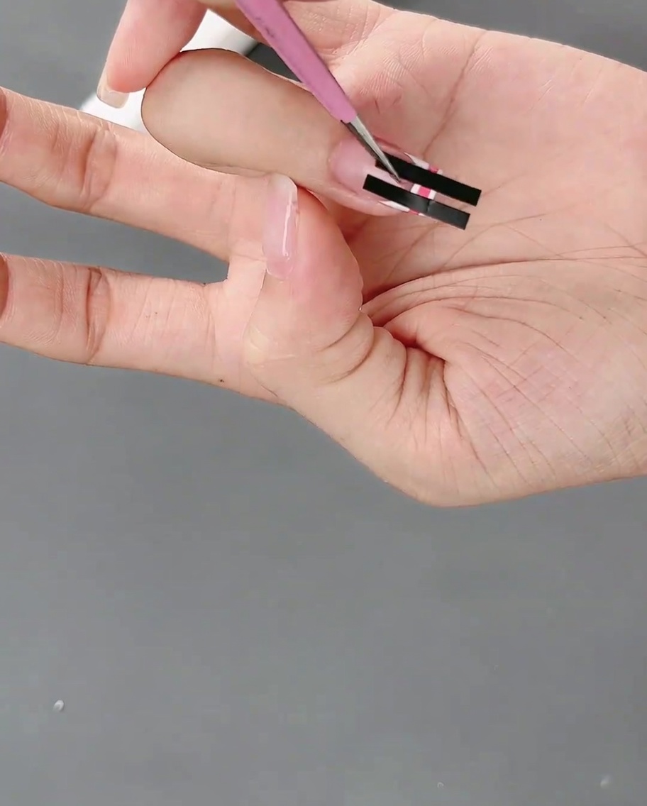 ピンセットでフレンチネイルステッカーをゆっくり剥がし、ピンクと白の格子模様が現れている様子。