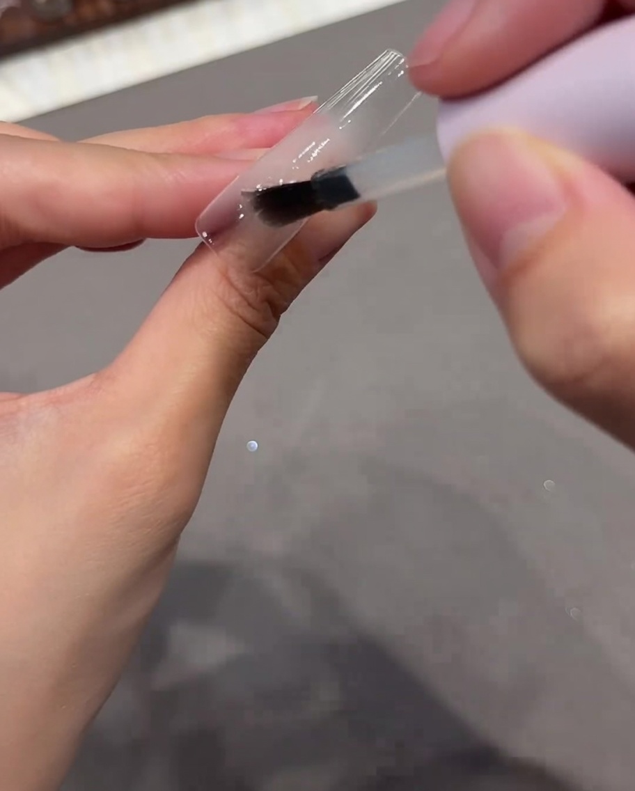 クリアネイルチップに透明なベースジェルをブラシで塗っている様子。