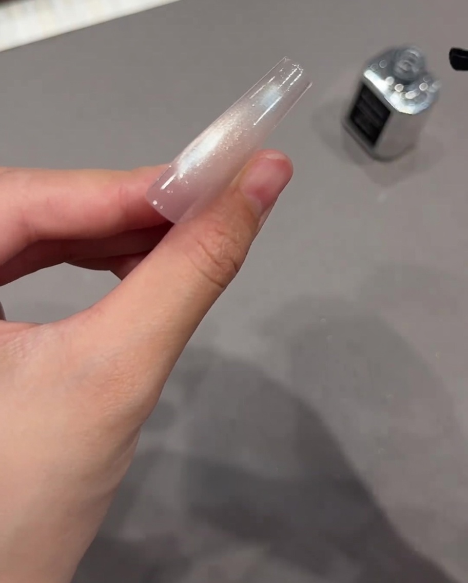 硬化後のキラキラしたキャッツアイネイルの上に透明なトップジェルを塗っている様子。