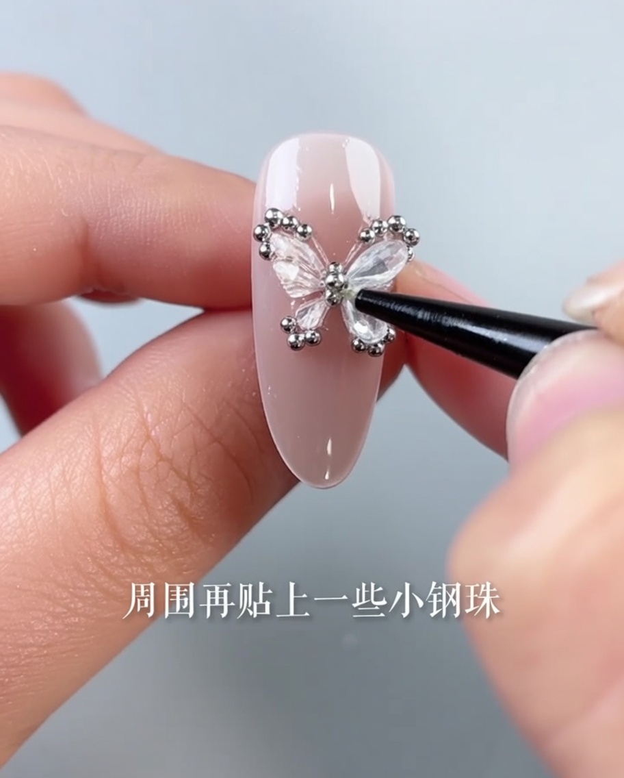 ピンセットを使って、蝶の周りに小さな銀色のスチールビーズを並べている様子。